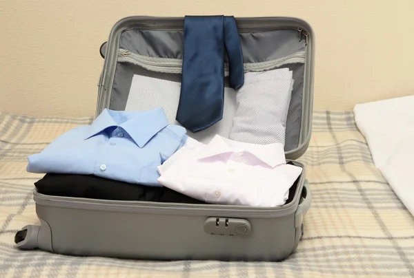 Maleta gris abierta con ropa en la cama — Foto de Stock