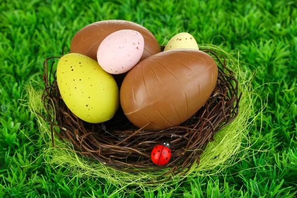 Composition of Easter and chocolate eggs in nest on grass background close-up — Stock Photo, Image