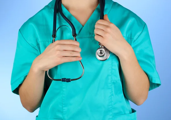 Médico com estetoscópio nas mãos sobre fundo azul — Fotografia de Stock