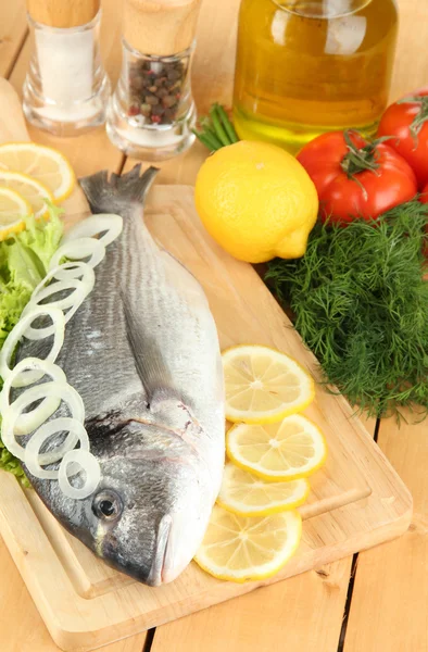 Dorado fresco sobre tabla de cortar con limón y verduras sobre mesa de madera — Foto de Stock