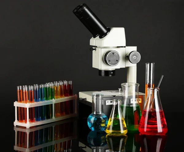 Provette con liquidi colorati e microscopio su fondo grigio scuro — Foto Stock