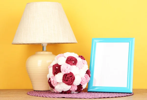 Cornice fotografica colorata, lampada e fiori su tavolo in legno su sfondo giallo — Foto Stock