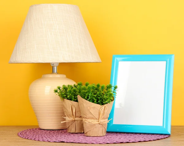 Bunter Fotorahmen, Lampe und Blumen auf Holztisch auf gelbem Hintergrund — Stockfoto