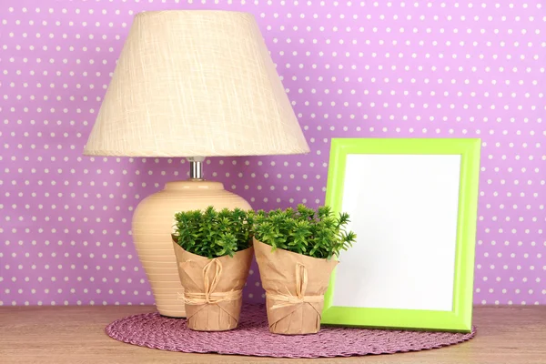 Moldura de foto colorida, lâmpada e flores na mesa de madeira em fundo de pontos de polca lilás — Fotografia de Stock