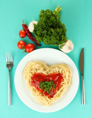 pişmiş spagetti dikkatle kalp şeklinde düzenlenmiş ve mavi zemin üzerine domates sosu ile tepesinde