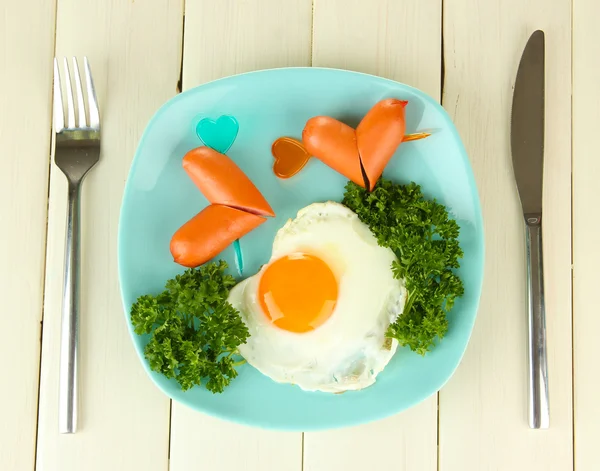 Sausages in form of hearts, scrambled eggs and parsley, on color plate, on wooden background — Stok fotoğraf