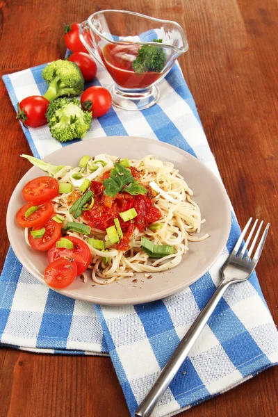 Spaghetti saporiti con salsa e verdure su piatto su tavolo di legno primo piano — Foto Stock