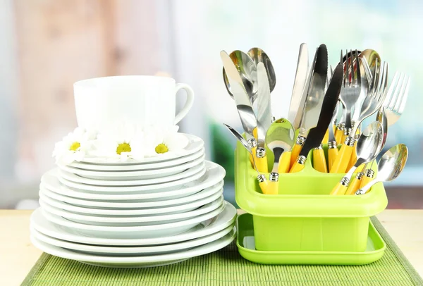 Placas, tenedores, cuchillos, cucharas y otros utensilios de cocina sobre estera de bambú, sobre fondo brillante — Foto de Stock