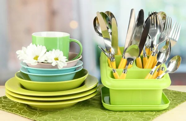 Piatti, forchette, coltelli, cucchiai e altri utensili da cucina su tovagliolo di colore, su sfondo brillante — Foto Stock