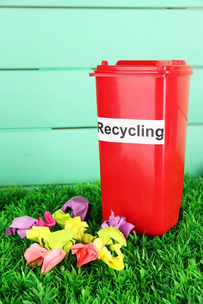 Papelera de reciclaje con papeles sobre hierba sobre fondo azul claro — Foto de Stock