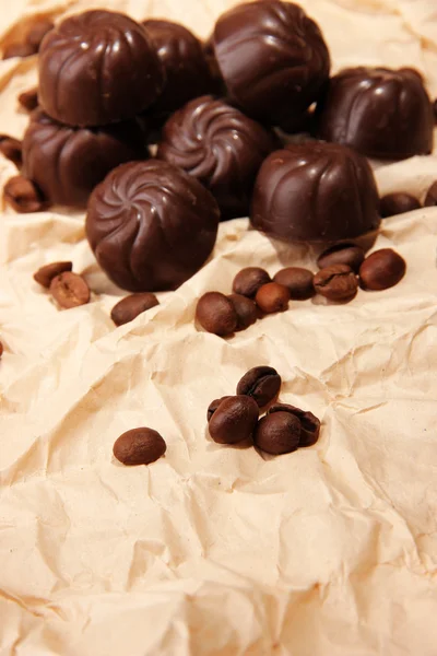 Doces de chocolate e grãos de café, sobre fundo de papel bege — Fotografia de Stock