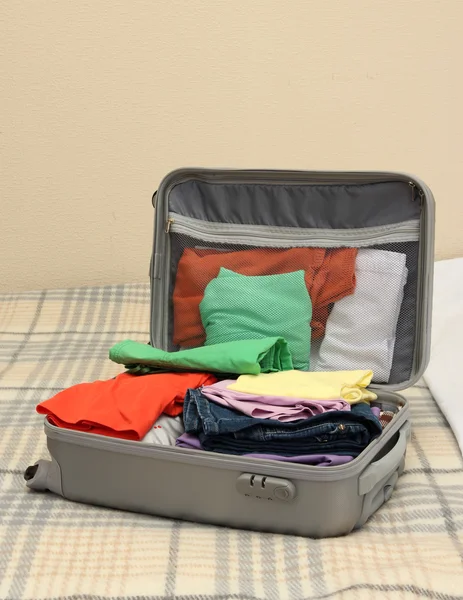 Open grey suitcase with clothing on bed — Stock Photo, Image