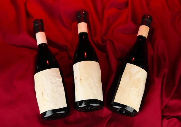 Botellas de vino sobre fondo de tela roja —  Fotos de Stock
