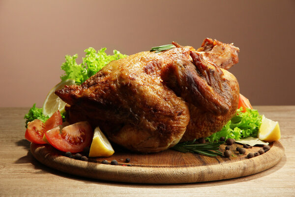 Whole roasted chicken with vegetables, on wooden table, on brown background