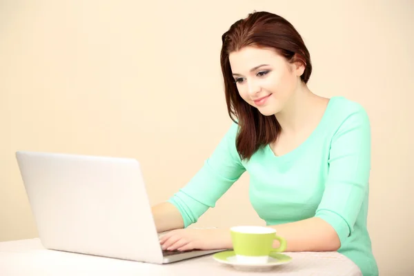 Mooie jonge vrouw die op laptop op lichte achtergrond werkt — Stockfoto