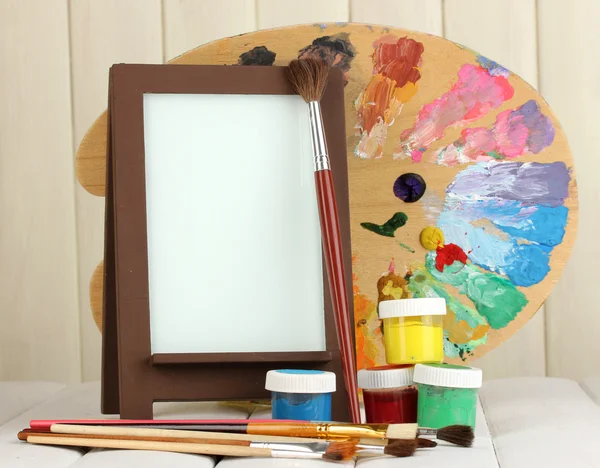 Photo frame as easel with artist's tools on wooden background — Stock Photo, Image