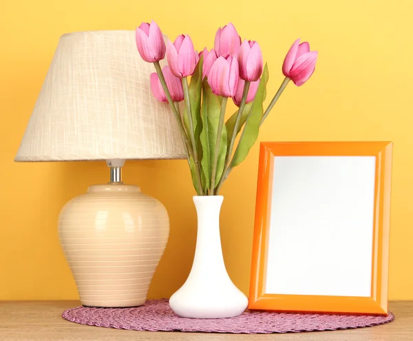 Cornice fotografica colorata, lampada e fiori su tavolo in legno su sfondo giallo — Foto Stock