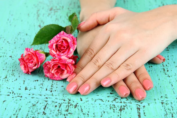 Mãos de mulher com manicure rosa e flores, em fundo de cor — Fotografia de Stock