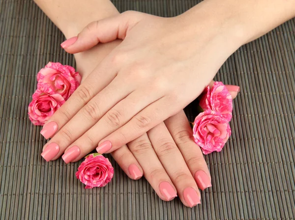 Manos de mujer con manicura rosa y flores, sobre fondo de estera de bambú — Foto de Stock