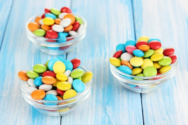 Kleurrijke snoepjes in glazen kommen op blauwe houten achtergrond — Stockfoto