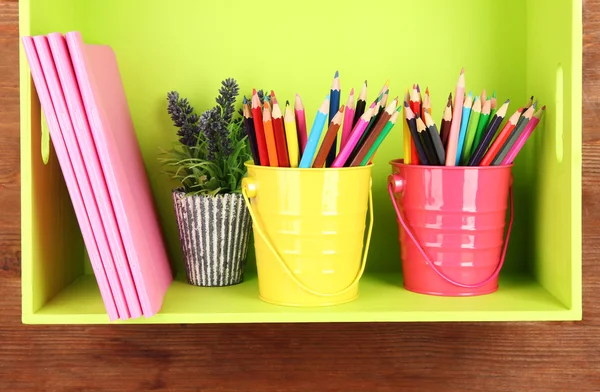 Kleurrijke potloden in emmers op plank met copybooks op houten achtergrond — Stockfoto