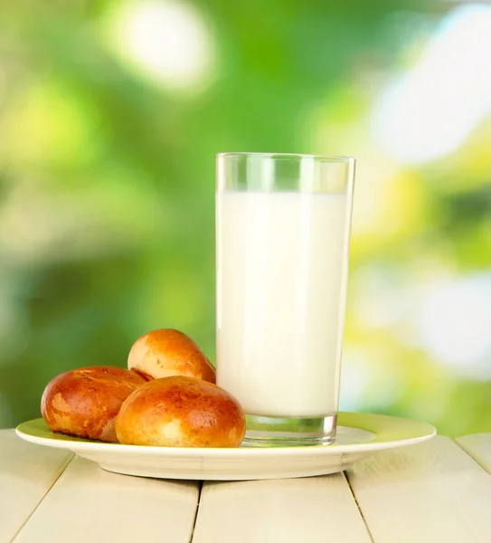 Panecillos y vaso de leche sobre mesa de madera sobre fondo natural — Foto de Stock