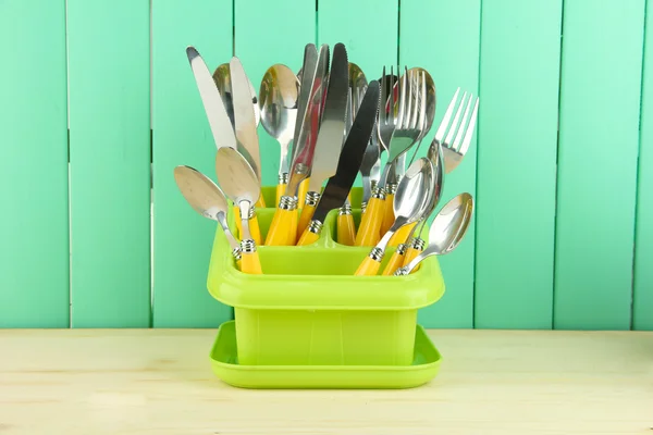 Cuchillos, cucharas, tenedores en recipiente de plástico para secar, sobre fondo de madera de color — Foto de Stock