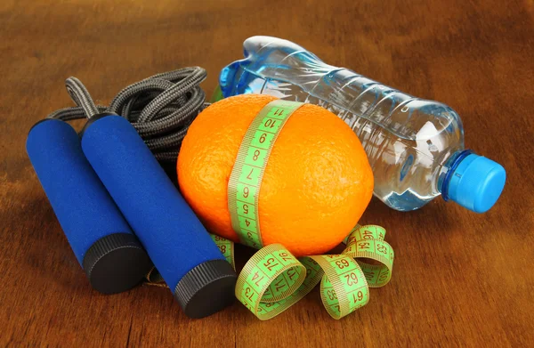 Orange with measuring tape,skipping rope and bottle of water, on wooden background — Stock Photo, Image
