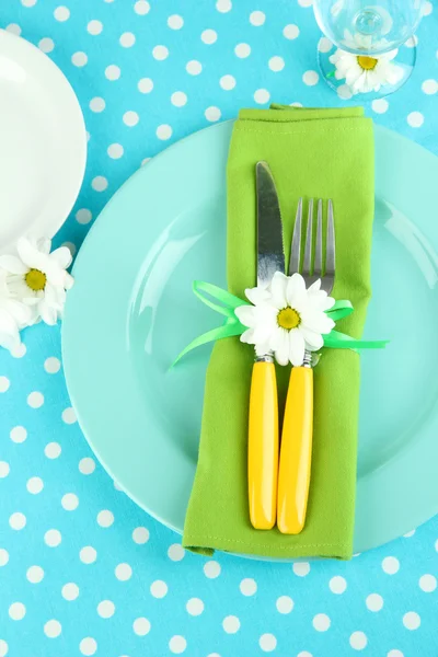 Coltello e forchetta avvolti in tovagliolo, su piatto, su sfondo tovaglia a colori — Foto Stock