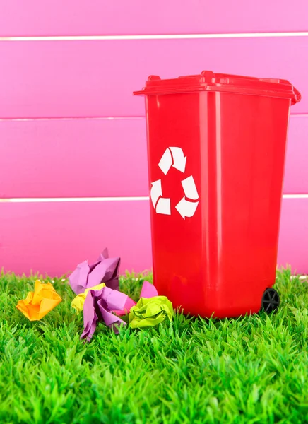 Cestino di riciclaggio con carte su erba su sfondo rosa — Foto Stock