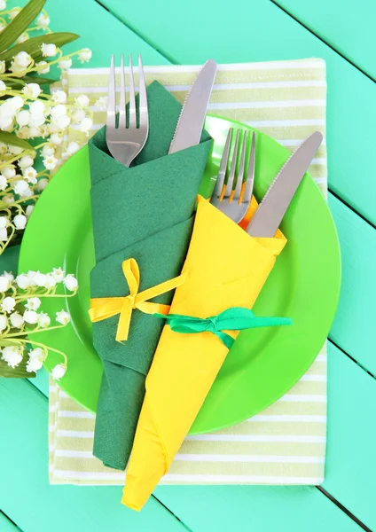 Forks and knives wrapped in green and yellow paper napkins, on color wooden background — Stock Photo, Image