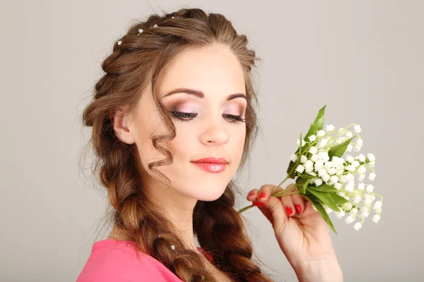 Mujer joven con hermoso peinado y flores, sobre fondo gris —  Fotos de Stock