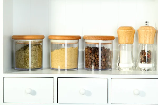 Beautiful white shelves with spices in glass bottles — Stock Photo, Image