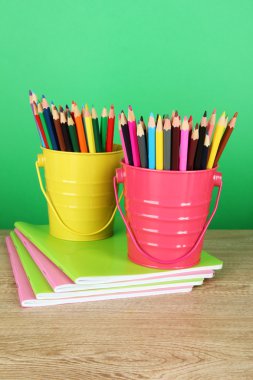 tabloda yeşil zemin üzerine copybooks ile iki kova içinde renkli kalemler