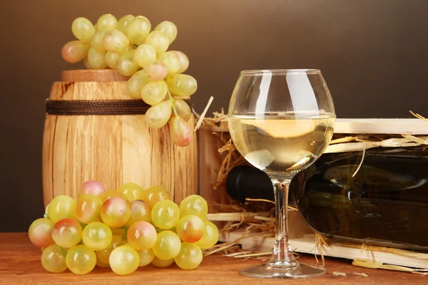 Caixa de madeira com garrafa de vinho, barril, vinho e uva em mesa de madeira sobre fundo marrom — Fotografia de Stock