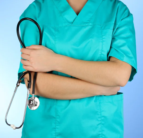 Médico com estetoscópio nas mãos sobre fundo azul — Fotografia de Stock