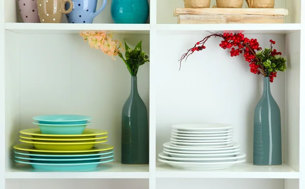 Prateleiras brancas bonitas com utensílios de mesa e deco — Fotografia de Stock