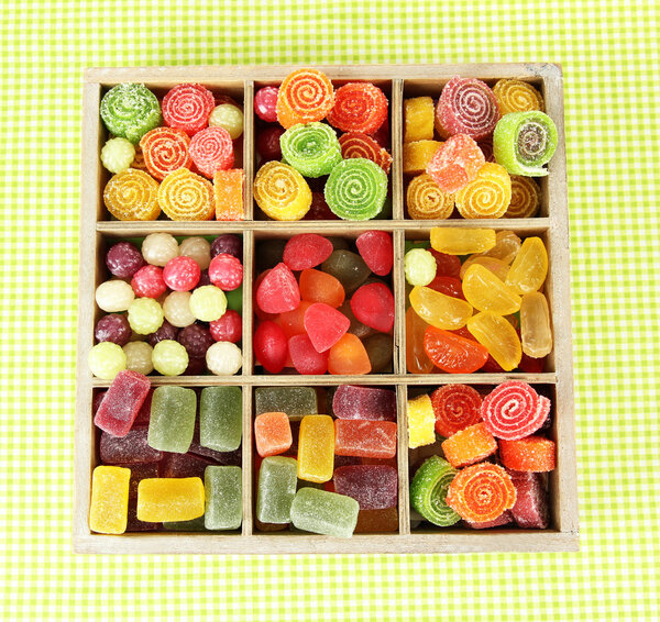 Multicolor candies in wooden box, on color background