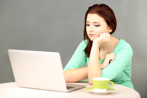 Schöne junge Frau arbeitet am Laptop auf grauem Hintergrund — Stockfoto