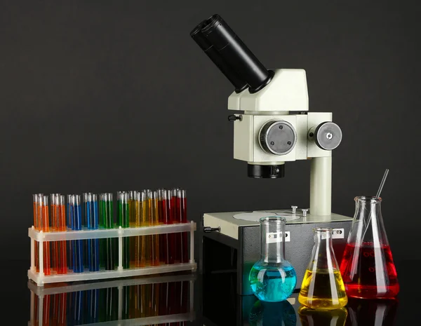 Tubos de ensayo con líquidos coloridos y microscopio sobre fondo gris oscuro — Foto de Stock