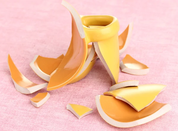 Copo quebrado amarelo na mesa no fundo rosa — Fotografia de Stock