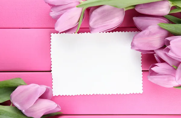 Belo buquê de tulipas roxas e cartão em branco no fundo de madeira rosa — Fotografia de Stock