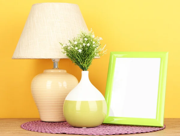 Cornice fotografica colorata, lampada e fiori su tavolo in legno su sfondo giallo — Foto Stock
