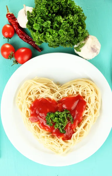 Gekookte spaghetti zorgvuldig gerangschikt in hart vorm en gegarneerd met tomatensaus, op blauwe achtergrond — Stockfoto