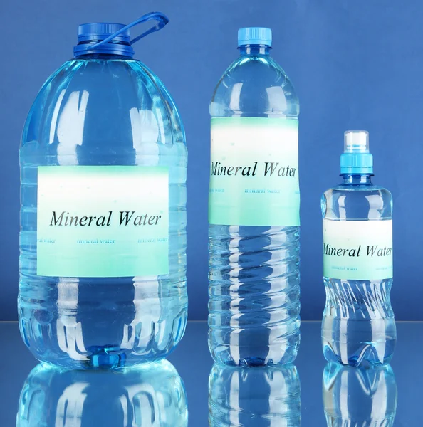 Frascos de água diferentes com etiqueta no fundo azul — Fotografia de Stock
