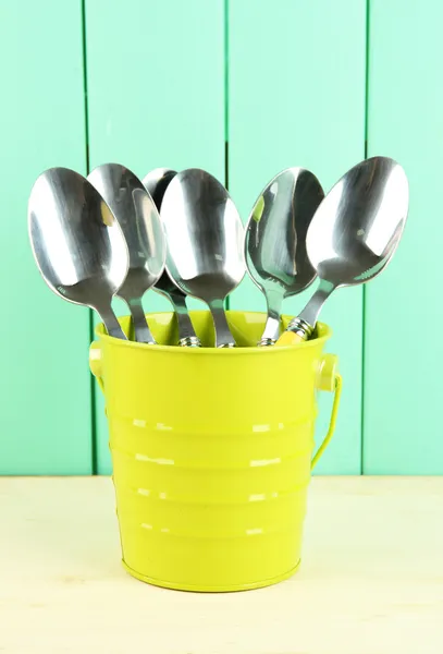 Spoons in metal bucket on color wooden background — Stock Photo, Image