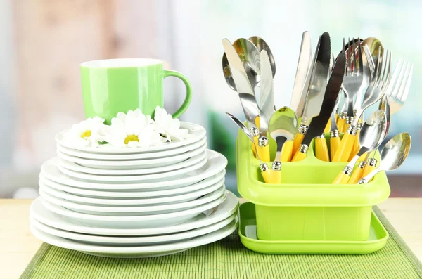 Placas, tenedores, cuchillos, cucharas y otros utensilios de cocina sobre estera de bambú, sobre fondo brillante — Foto de Stock