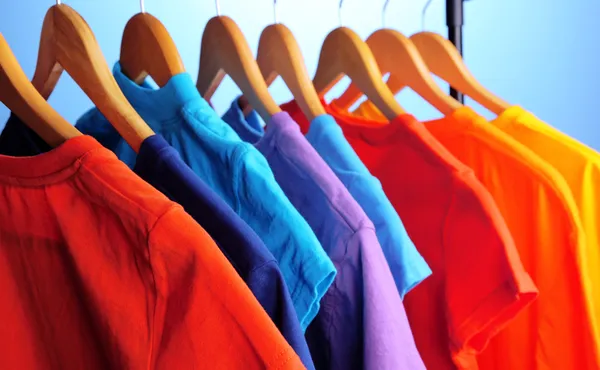 Lots of T-shirts on hangers on blue background — Stock Photo, Image