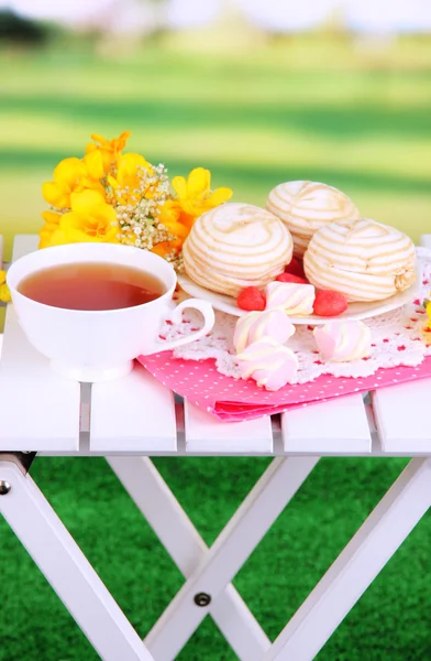 Beautiful composition with cup of tea and marshmallow on wooden picnic table on natural background — Stock Photo, Image