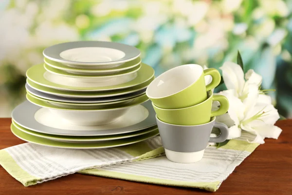 Leere Teller und Tassen auf Holztisch auf grünem Hintergrund — Stockfoto